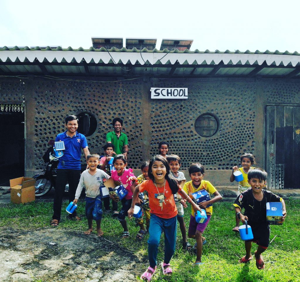 Cambodian children running with solar lamps in front of the recycled bottle-brick school at the Red Road Foundation